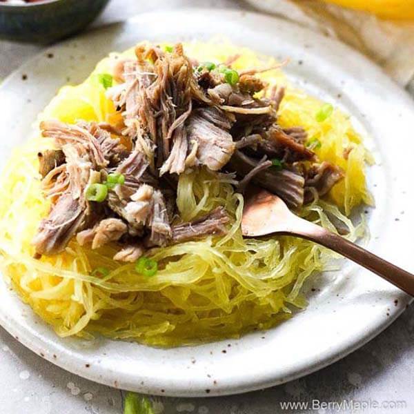 berry maple pork over spaghetti squash with a fork on a white plate with black speckles