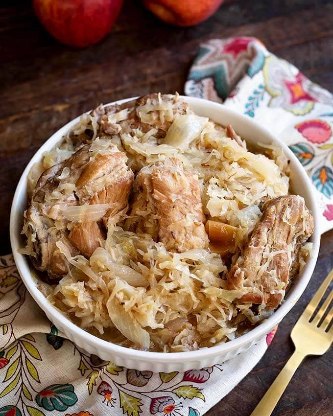 Pork and Sauerkraut in a white bowl next to a gold fork on a floral napkin