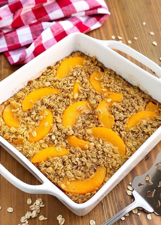 Peach Baked Oatmeal in a white square baking dish next to a red gingham napkin