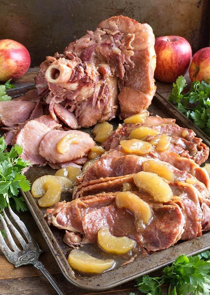 Sliced Apple Pie Ham on a baking sheet next to fresh herb bunches