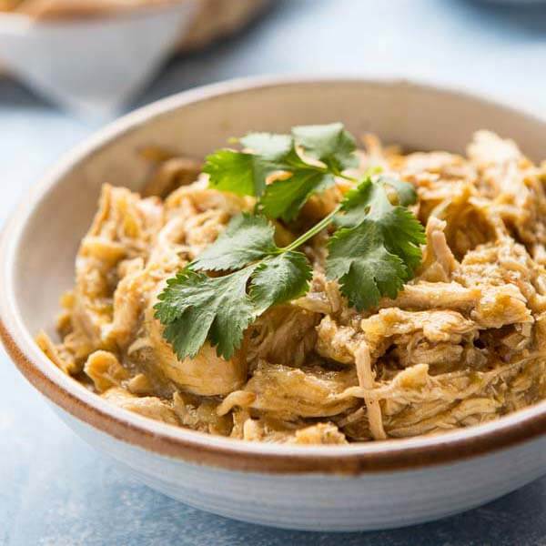 chicken chili in a white bowl with brown rim topped with fresh green herb