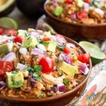 Two Chicken Taco Bowls in brown bowls topped with diced red onion, avocado, and cherry tomatoes