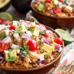 Two Chicken Taco Bowls in brown bowls topped with diced red onion, avocado, and cherry tomatoes