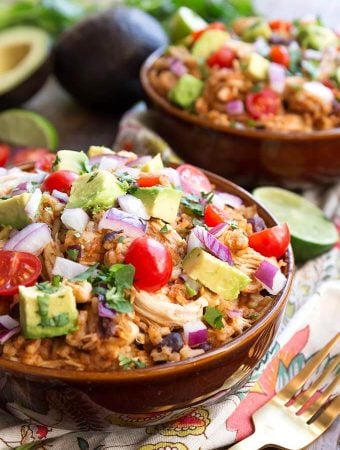 Two Chicken Taco Bowls in brown bowls topped with diced red onion, avocado, and cherry tomatoes