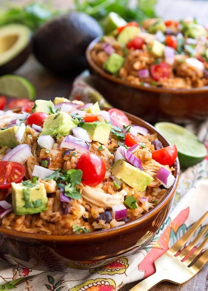 Two Chicken Taco Bowls in brown bowls topped with diced red onion, avocado, and cherry tomatoes