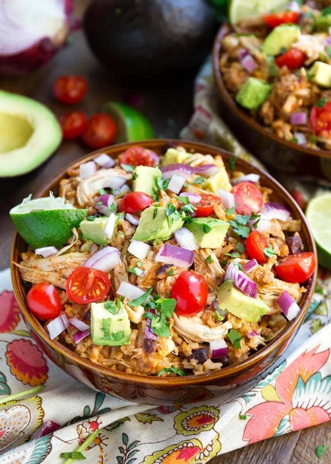 Two Chicken Taco Bowls in brown bowls topped with diced red onion, avocado, and cherry tomatoes