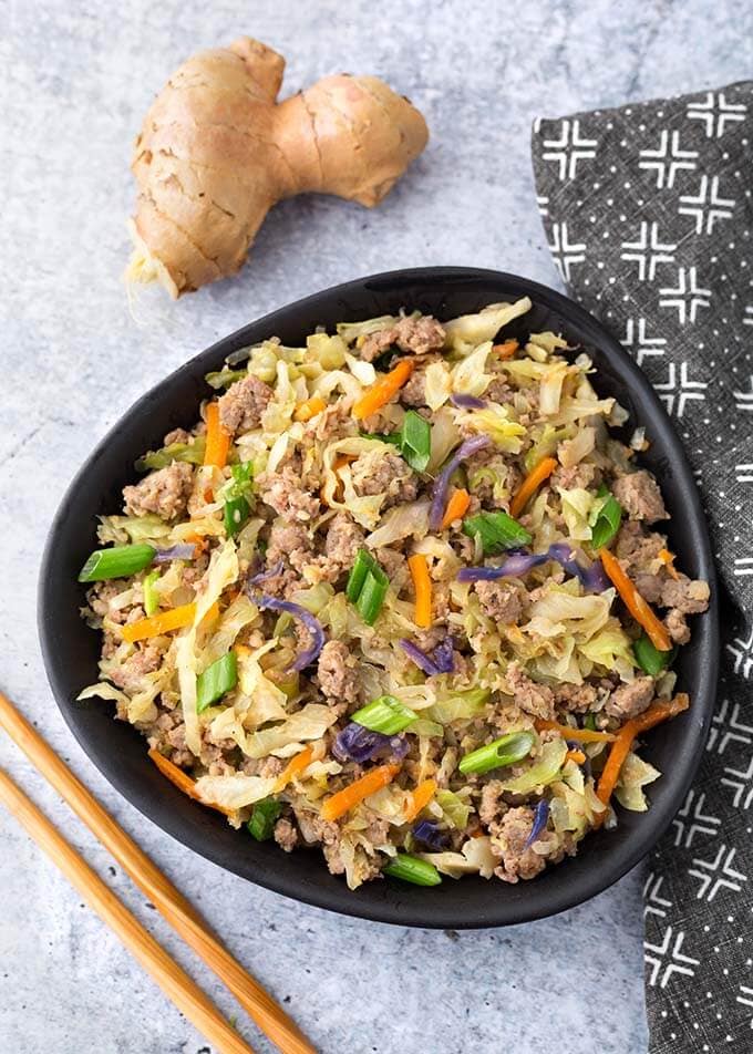 Egg roll in a bowl in a black bowl next to two wooden chopsticks and ginger root