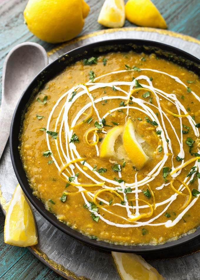 Red Lentil Curry Soup in a black bowl on a silver platter next to a silver spoon and lemon slices