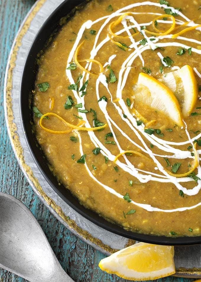 Red Lentil Curry Soup in a black bowl which is on a silver platter garnished with cream and lemon slices