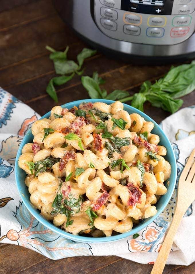 Tuscan Chicken Pasta in a blue bowl in front of a pressure cooker