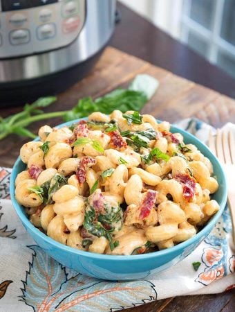 Tuscan Chicken Pasta in a blue bowl in front of a pressure cooker