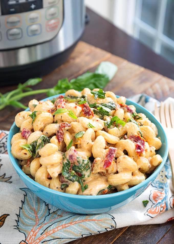 Tuscan Chicken Pasta in a blue bowl in front of a pressure cooker