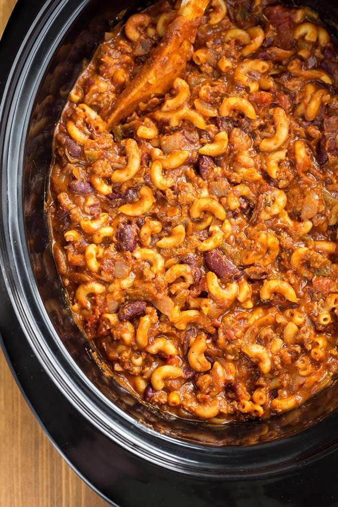 Top view of Chili Mac and wooden mixing spoon in a slow cooker