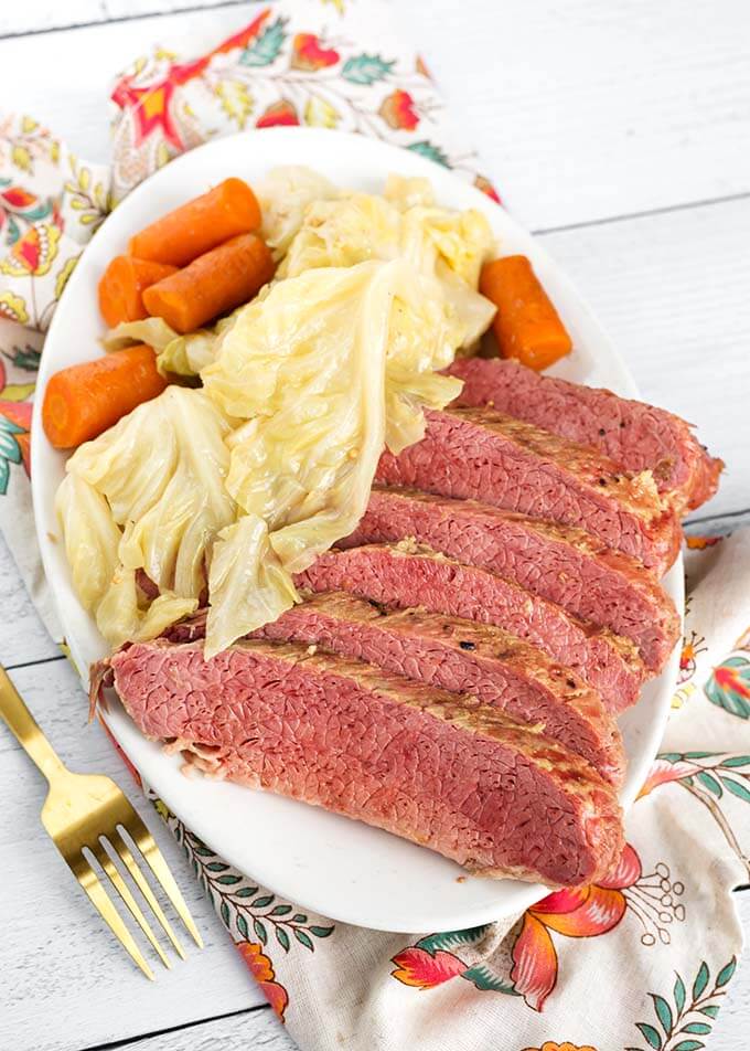 Corned Beef and Cabbage with carrots on a white oblong plate next to a gold fork