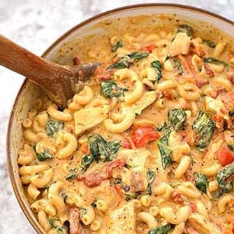 creamy garlic tuscan chicken pasta and a wooden spoon in a white bowl with a brown rim