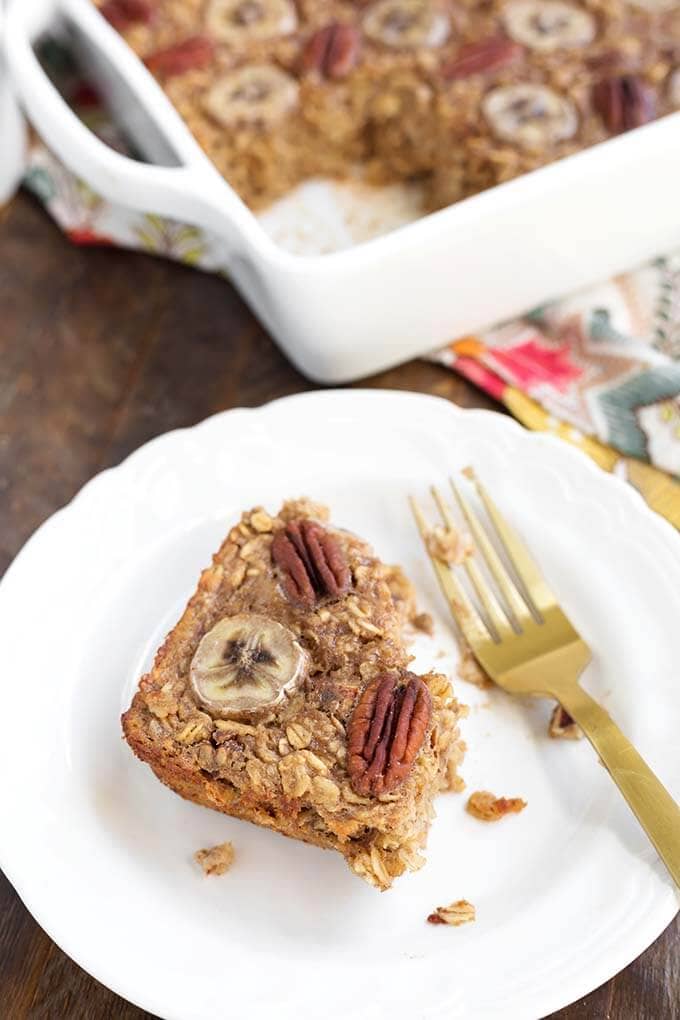 Partially eaten slice of Baked Oatmeal on white dish with gold fork