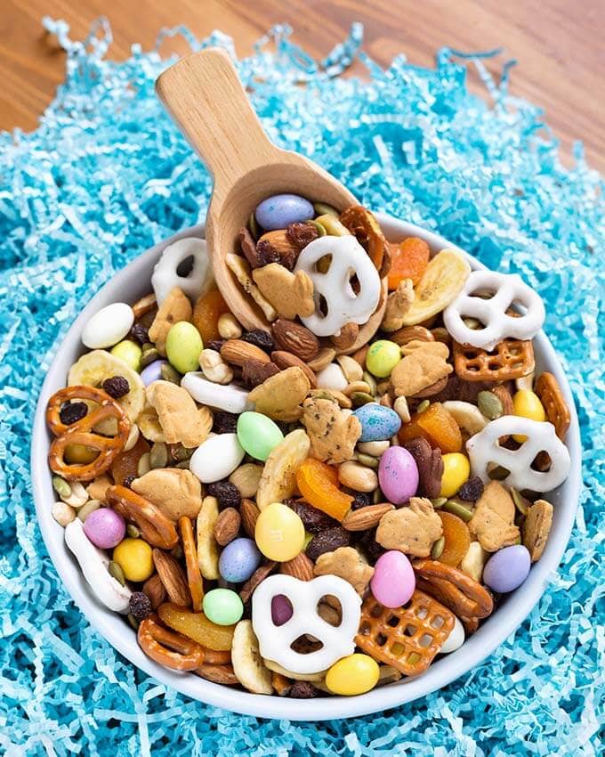 Bunny Bait Easter Trail Mix in a white bowl with wooden serving spoon on top of shredded light blue confetti paper