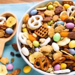 Bunny Bait Easter Trail Mix in a white bowl next to a wooden serving spoon all on a blue napkin