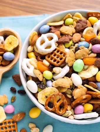Bunny Bait Easter Trail Mix in a white bowl next to a wooden serving spoon all on a blue napkin