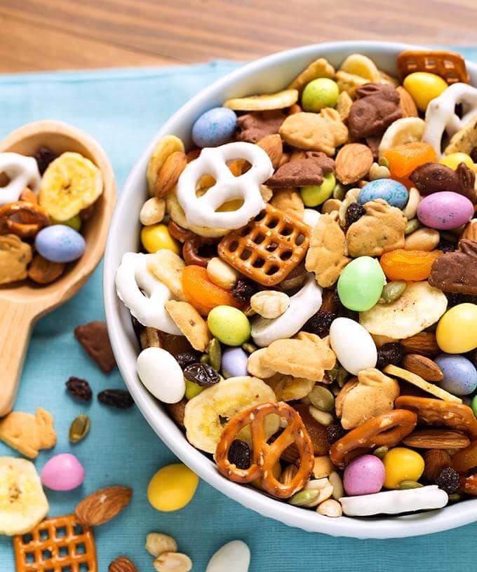 Bunny Bait Easter Trail Mix in a white bowl next to a wooden serving spoon all on a blue napkin