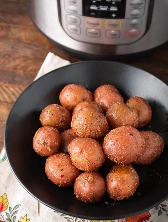Baby Potatoes on a black plate in front of a pressure cooker
