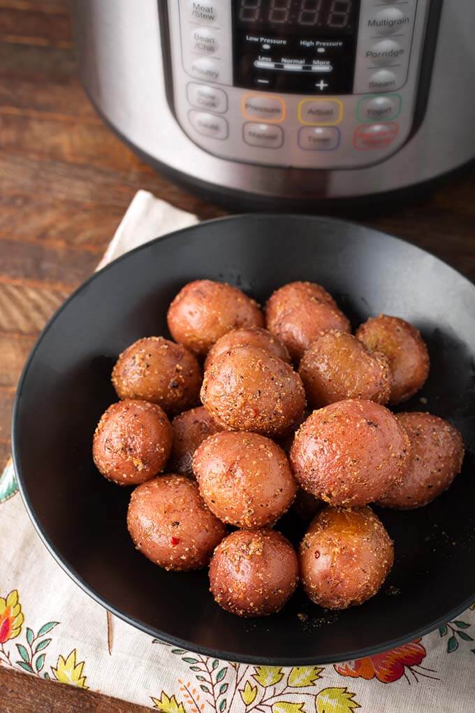 Baby Potatoes on a black plate in front of Pressure cooker