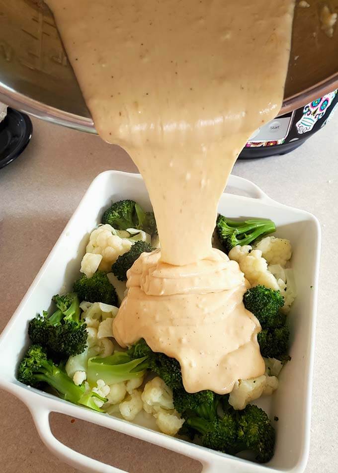 broccoli and cauliflower in a white baking dish with cheese sauce pouring over them