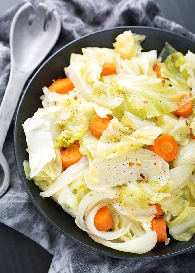 Cabbage Side Dish in a black bowl next to a silver fork all on a gray napkin