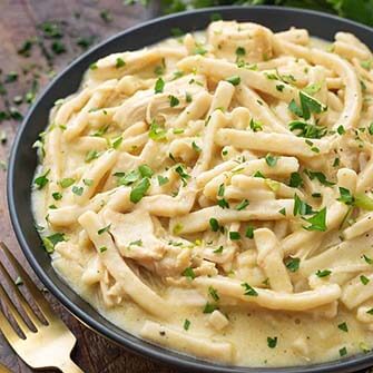 chicken noodles on a black plate next to a gold fork on a wooden surface