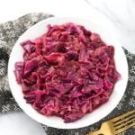 German Red Cabbage on a white plate next to golden fork on top of a black patterned napkin