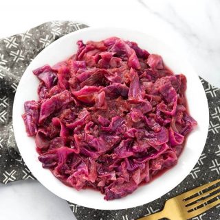 German Red Cabbage on a white plate next to golden fork on top of a black patterned napkin