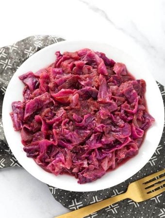 German Red Cabbage on a white plate next to golden fork on top of a black patterned napkin