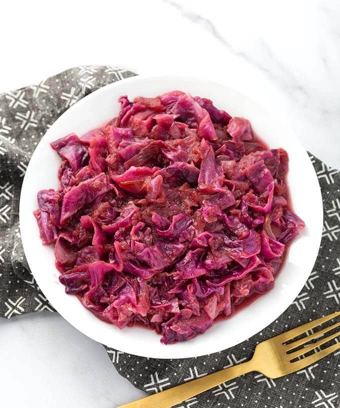 German Red Cabbage on a white plate next to golden fork on top of a black patterned napkin