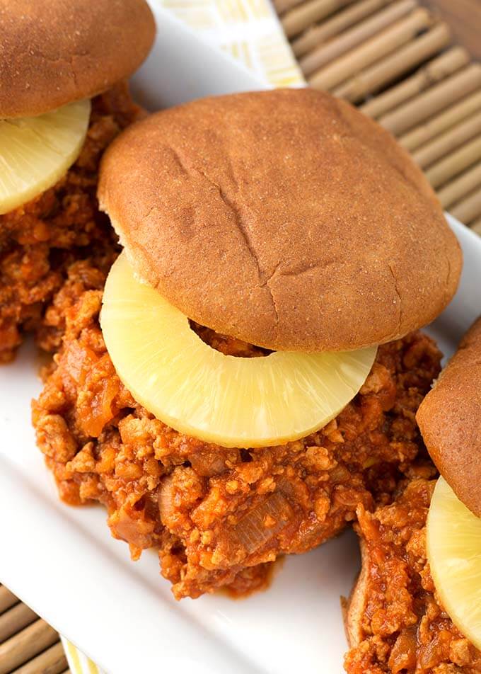 Three Hawaiian BBQ Sloppy Joes with slices of pineapples on hamburger buns on a white serving platter