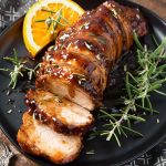 Sliced Honey Garlic Pork Tenderloin garnished with fresh rosemary on black plate