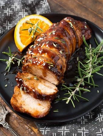 Sliced Honey Garlic Pork Tenderloin garnished with fresh rosemary on black plate