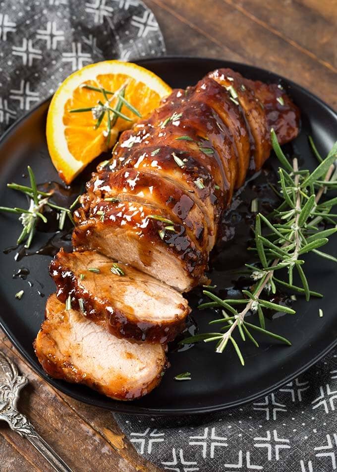 Sliced Honey Garlic Pork Tenderloin with rosemary garnish on black plate