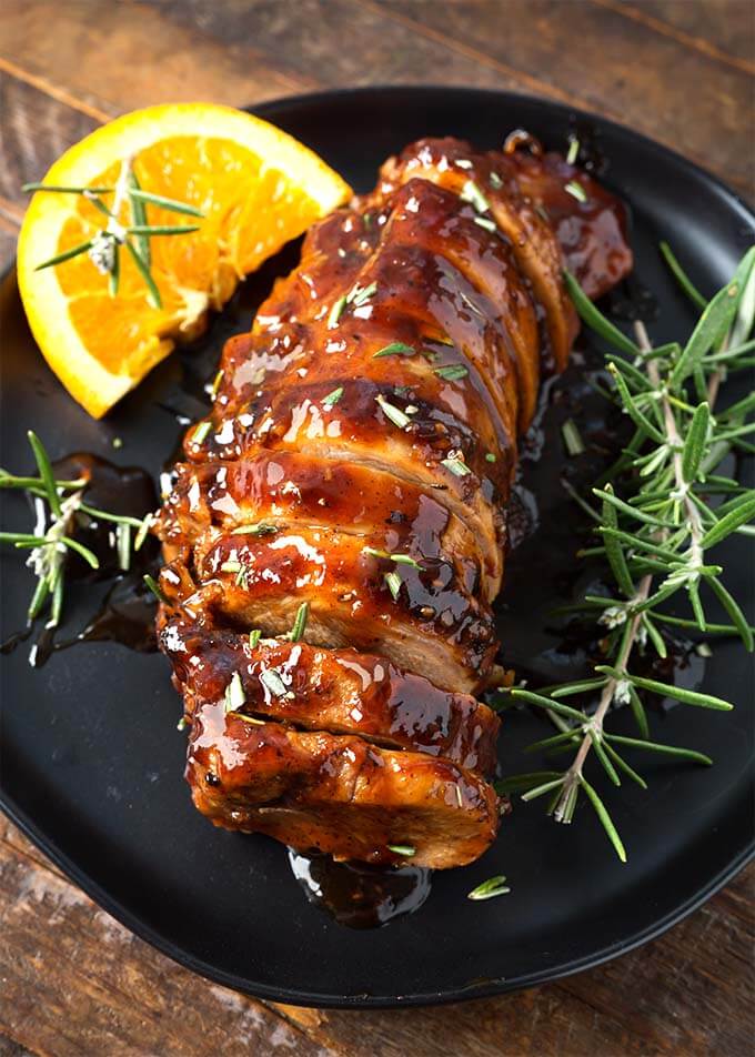 Sliced Honey Garlic Pork Tenderloin with rosemary garnish on black plate