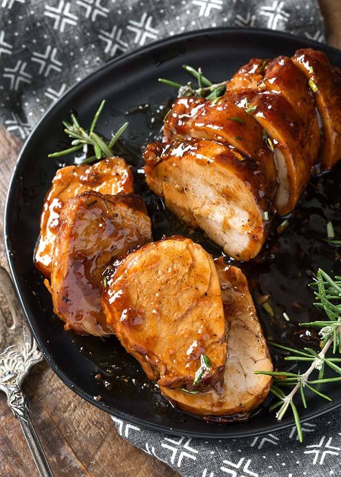Sliced Honey Garlic Pork Tenderloin with rosemary garnish on black plate