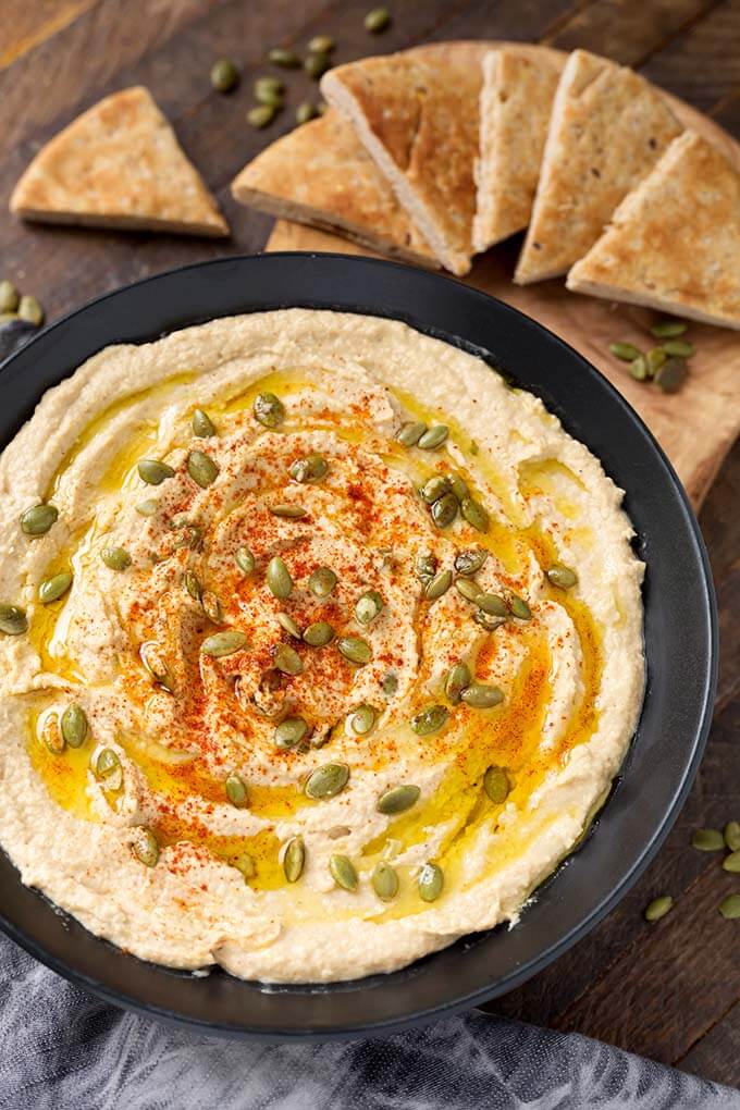 Hummus in a black bowl next to wooden board with cut pieces of flatbread