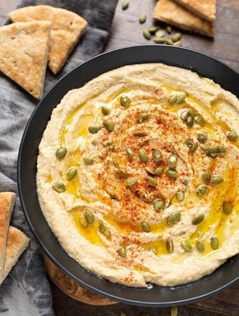 Hummus in black bowl next to cut pieces of flatbread