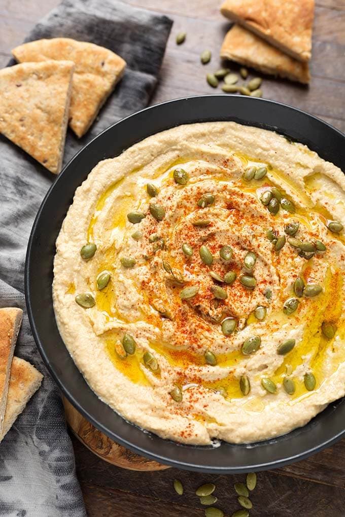Hummus in a black bowl surrounded by triangular pieces of flatbread