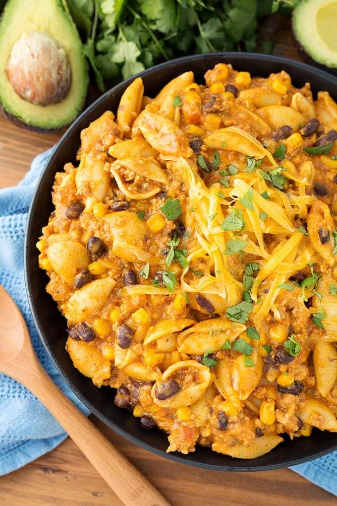 Loaded Taco Pasta on black plate next to wooden spoon and avocados