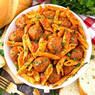 meatball pasta dinner on a white plate next to sliced french bread