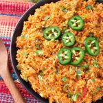 Mexican Rice on a black plate on top of a red and blue stripped mat