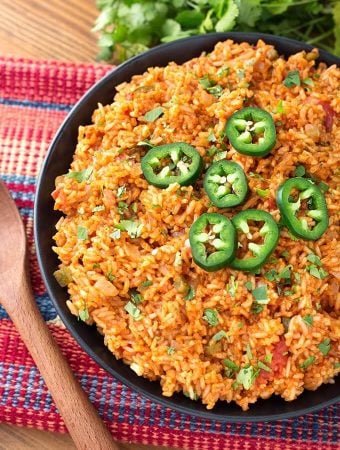 Mexican Rice on a black plate on top of a red and blue stripped mat