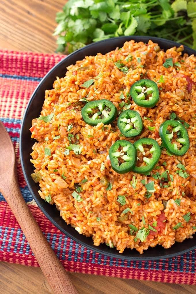 Mexican Rice topped with sliced jalapeno on a black plate next to a wooden spoon