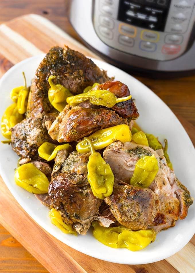 Mississippi Pork on white serving platter on a wooden board in front of a pressure cooker