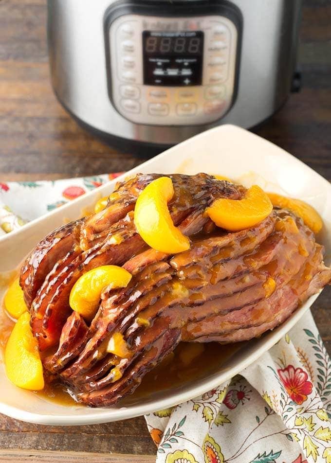 Peach Glazed Ham on white serving platter in front of pressure cooker