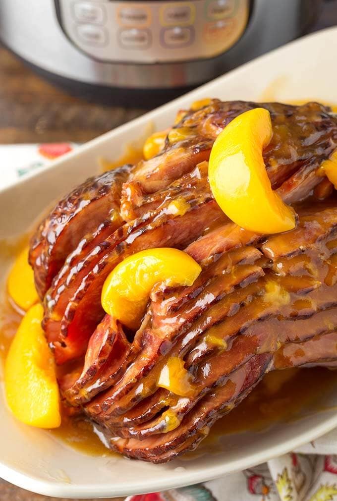 Peach Glazed Ham on white serving platter in front of pressure cooker